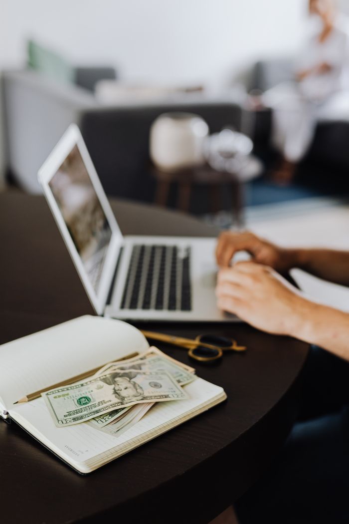 Woman working remotely on a laptop with money on a notebook, ideal for business or finance themes.